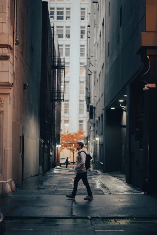 Free A man with a backpack walks through a dimly lit alleyway in Seattle at dusk, capturing urban tranquility. Stock Photo