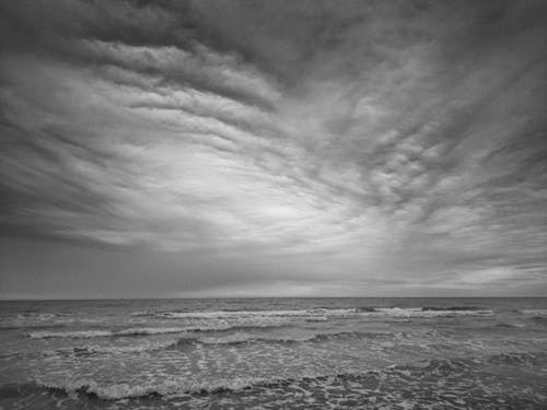 A Grayscale Photo of an Ocean Under the Cloudy Sky