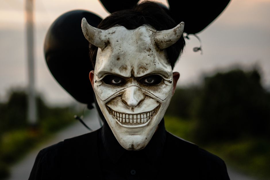 A haunting masked figure with black balloons outdoors, evoking a thrilling and eerie atmosphere.