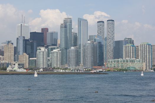 A stunning view of Toronto's skyscrapers reflecting on Lake Ontario under a blue sky.