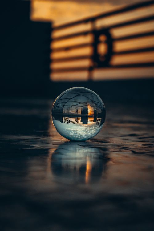 Free A glass crystal ball reflects a sunset on a concrete surface, creating an artistic scene. Stock Photo