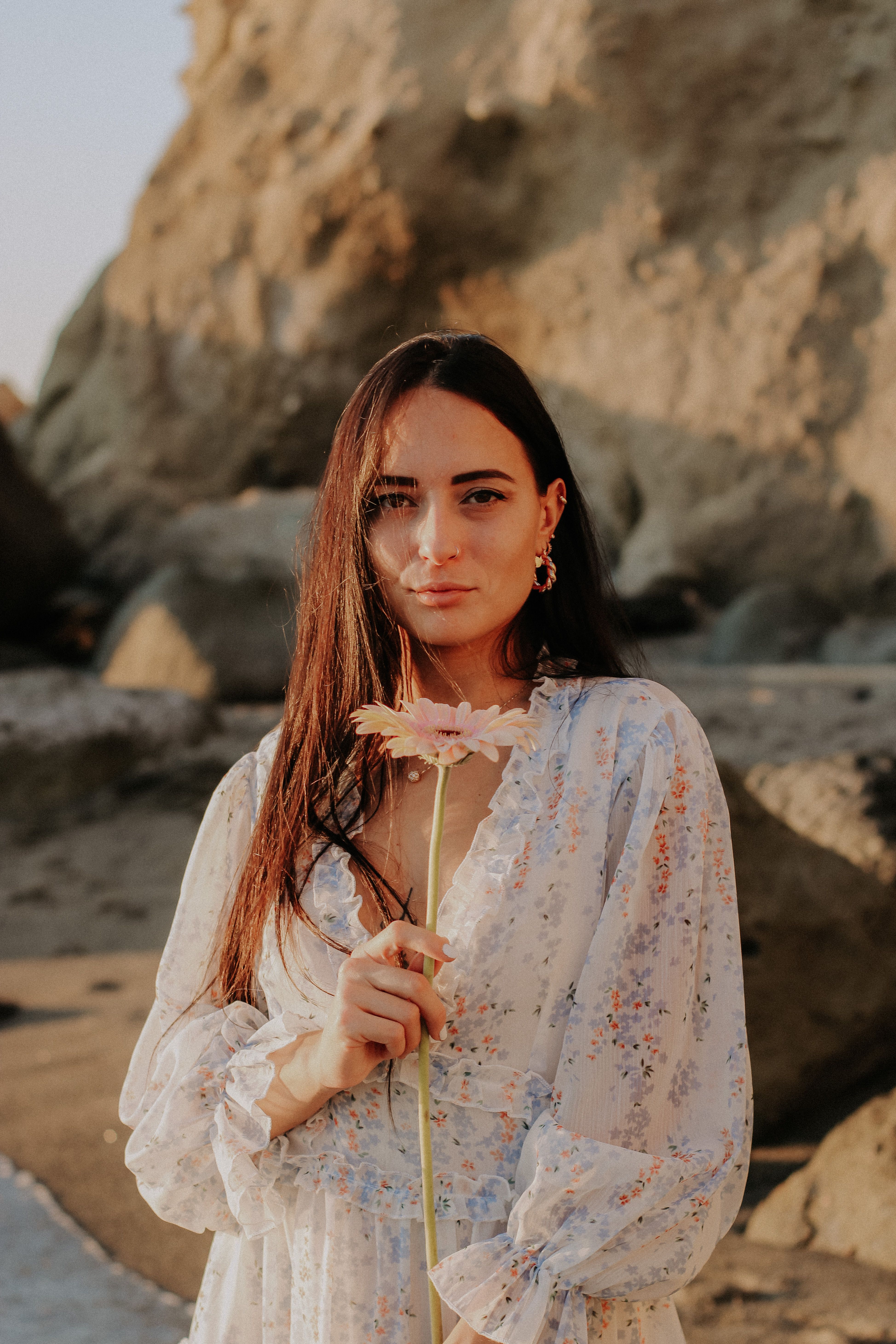 Young woman with long hair holding a flower on a sunny beach.