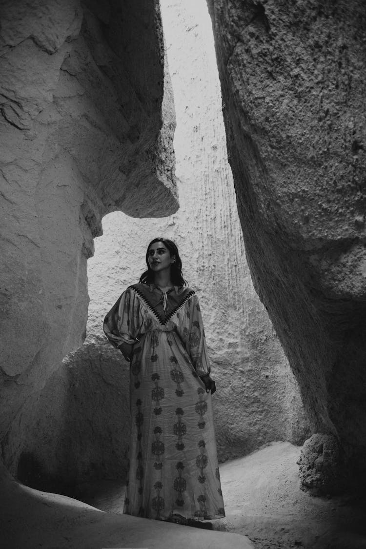 A Grayscale Of A Woman Wearing A Dress In A Cave