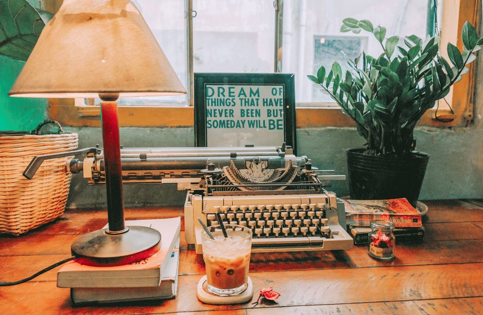 A cozy vintage workspace featuring a typewriter, lamp, and iced coffee.