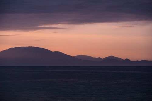 Free Idyllic view of ocean and mountains silhouetted during sunset, creating a serene landscape. Stock Photo