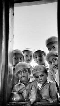 A group of children in traditional attire gazing through a window with solemn expressions.