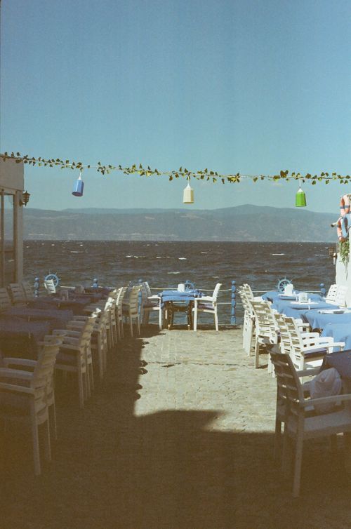 Free Outdoor coastal restaurant with tables and chairs overlooking the sea under a clear summer sky. Stock Photo