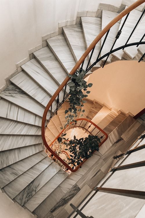 Free Stylish spiral staircase with marble steps and lush greenery, creating an elegant interior. Stock Photo