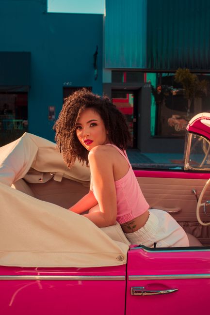 Stylish woman sits in a vibrant pink convertible, exuding confidence and glamour.