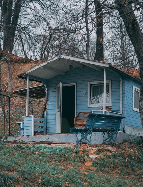 Free Charming blue cabin surrounded by bare trees in a serene autumn forest setting. Stock Photo