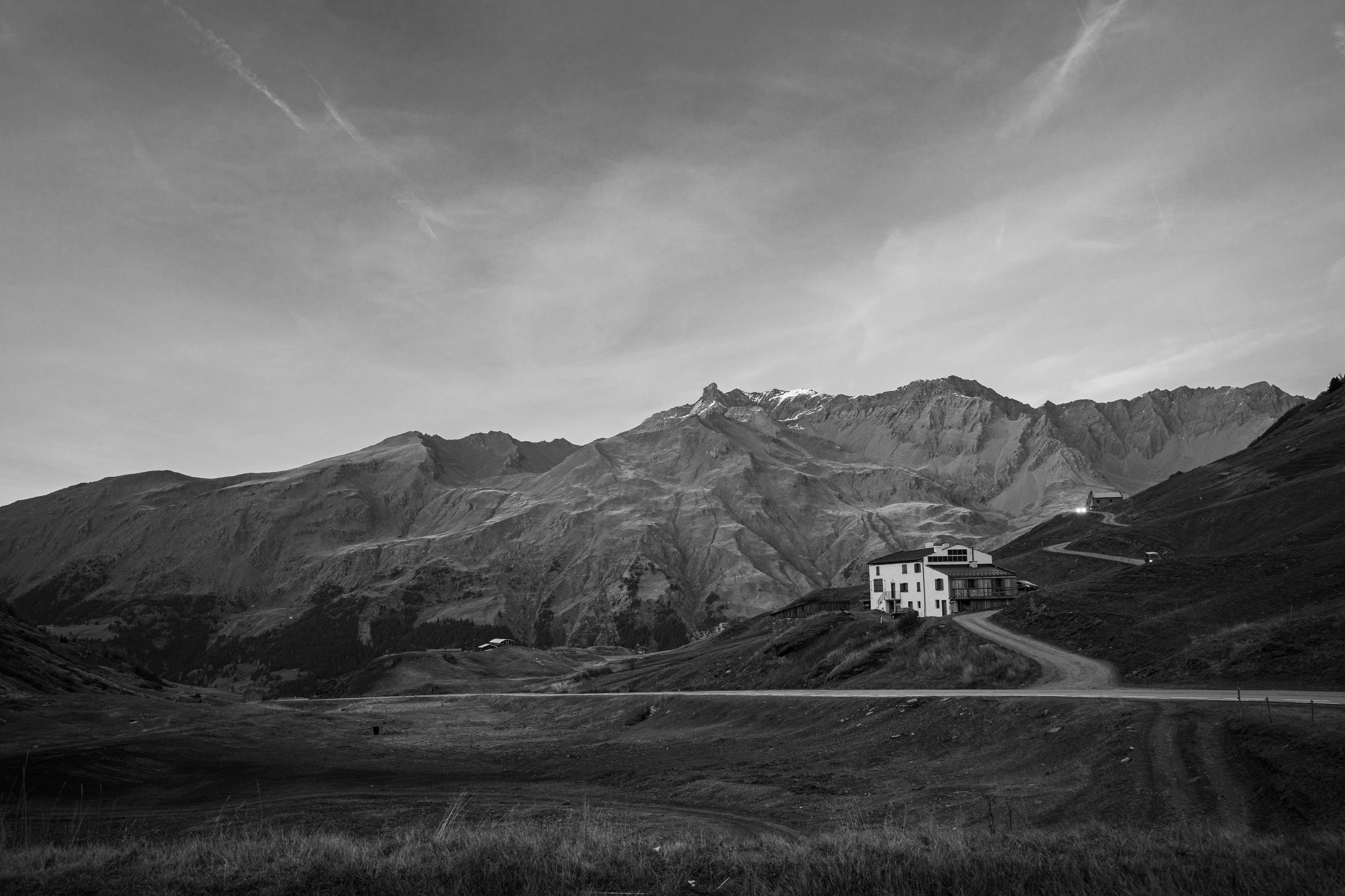 A solitary house nestled in a vast mountain landscape under a wide sky.
