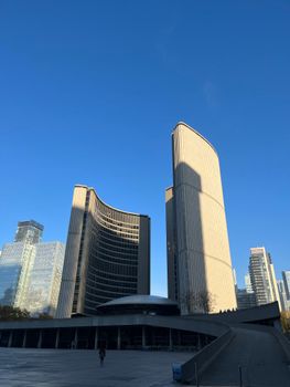 Low angle view of iconic Toronto City Hall under a clear blue sky, showcasing modern architecture.