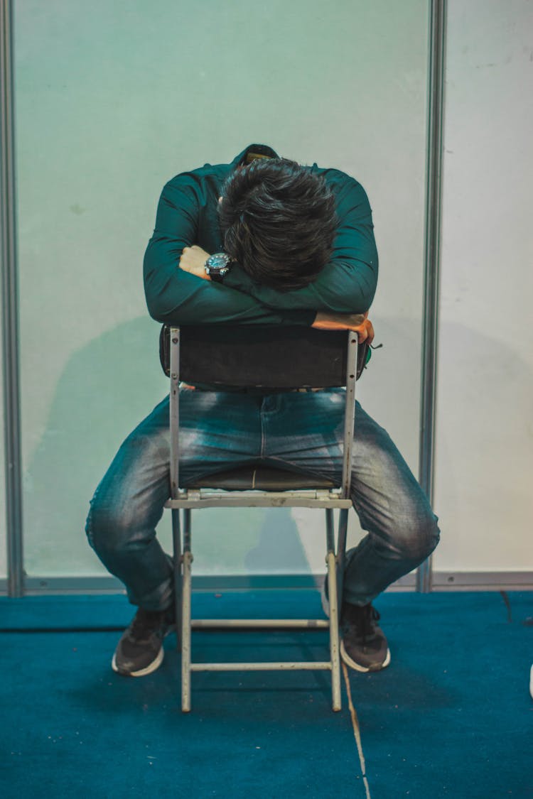 Man Sitting Hiding Face In Hands Resting On The Back Of Chair