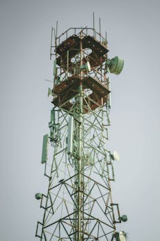 Steel communication tower with satellite dishes against a clear sky.