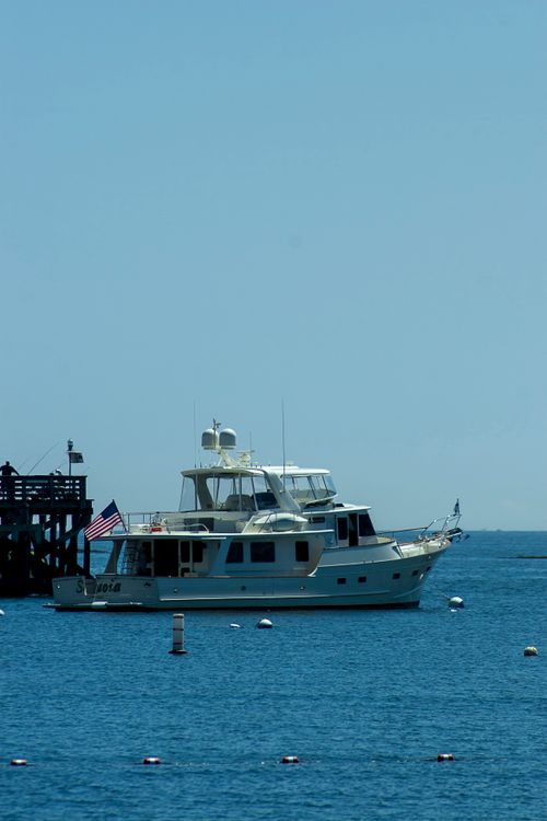 Free An elegant yacht with an American flag on calm blue waters beside a wooden dock. Stock Photo