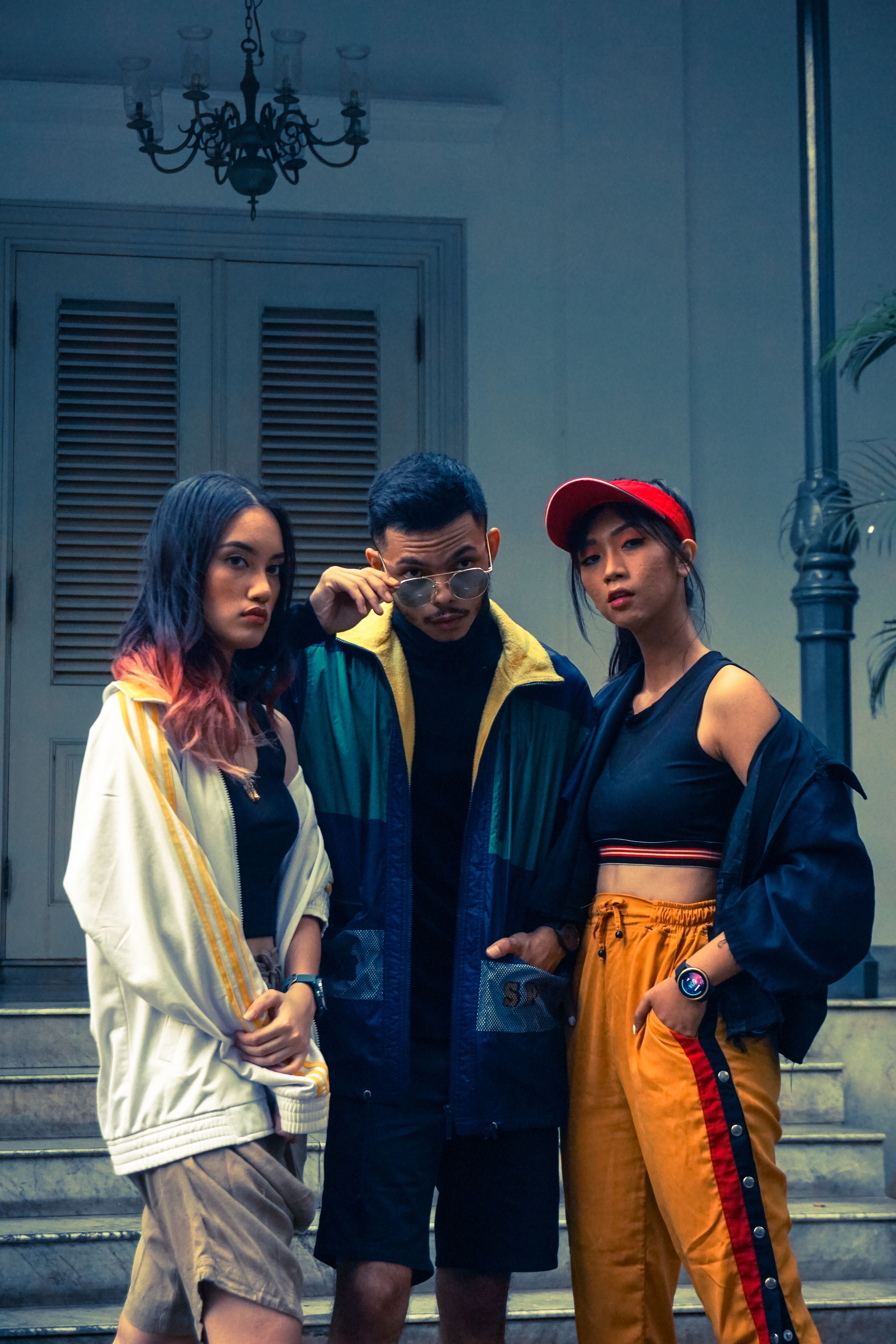 Três jovens adultos posando de maneira estilosa ao ar livre em roupas urbanas com cores vibrantes.