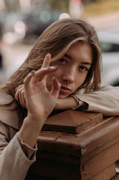 A contemplative woman with long brown hair is resting her head on her hand, gazing intently outdoors.
