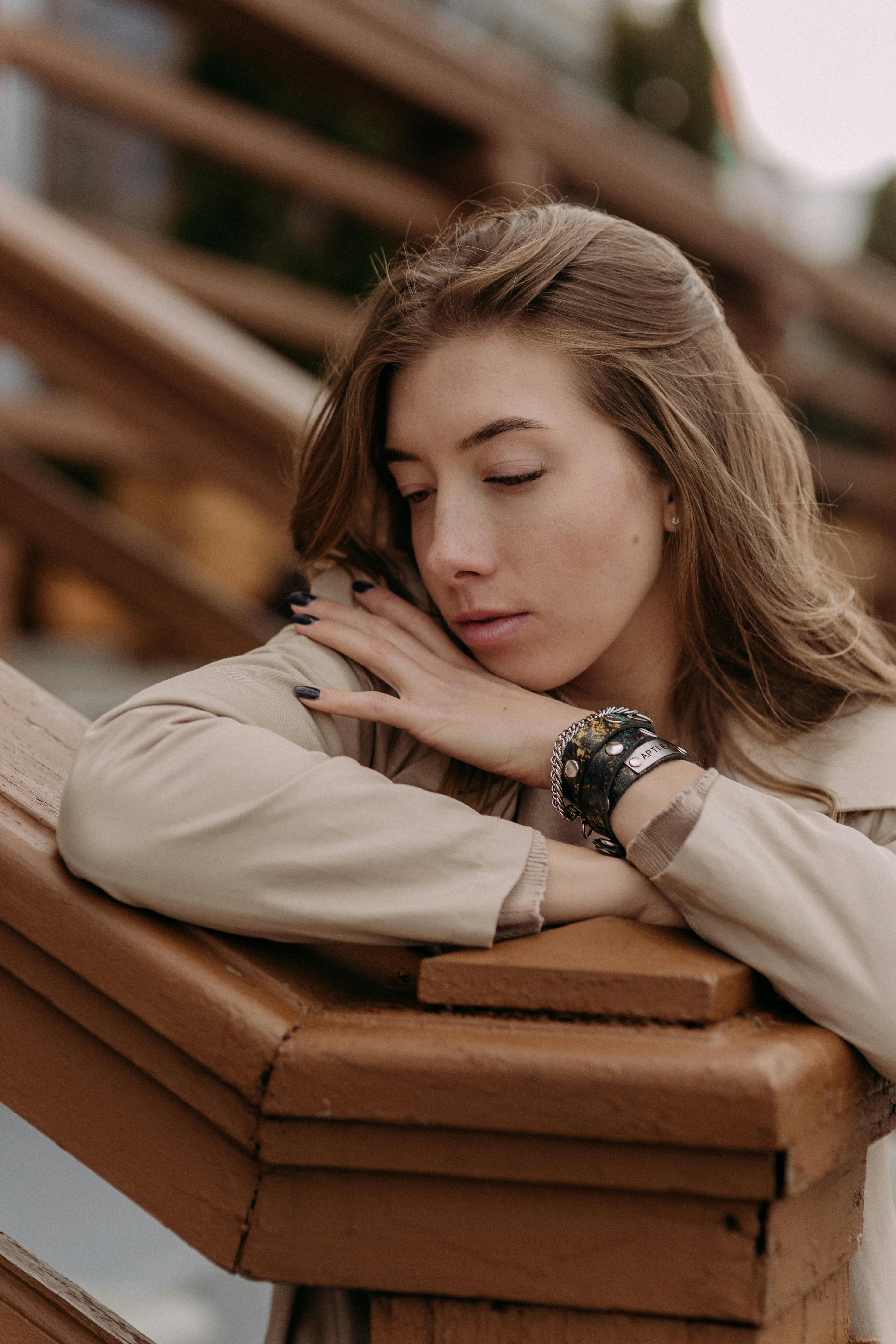 Thoughtful woman with brown hair relaxes on a wooden handrail, conveying a peaceful mood.