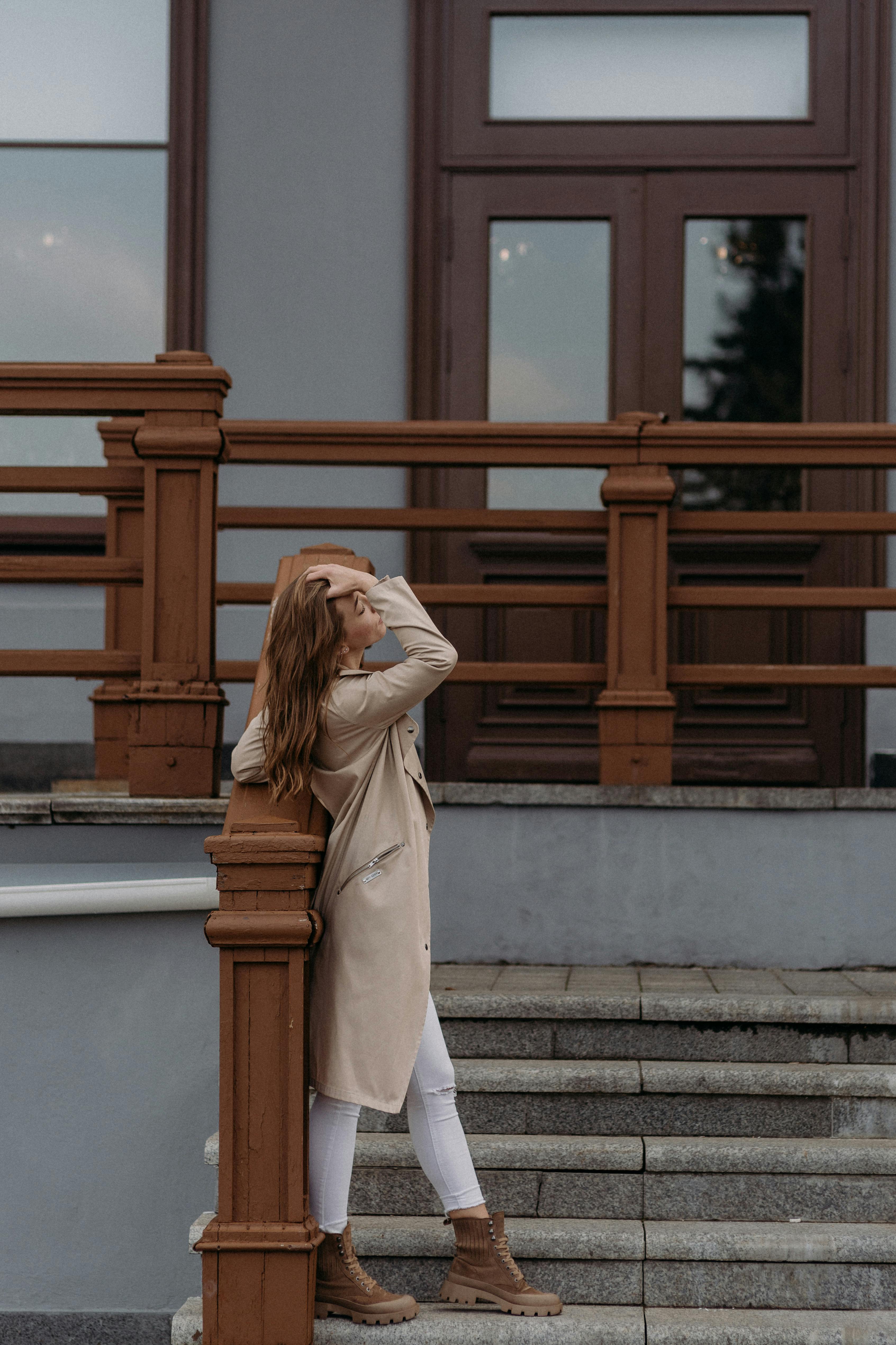 Profile view of a woman in a brown coat leaning on staircase railing.