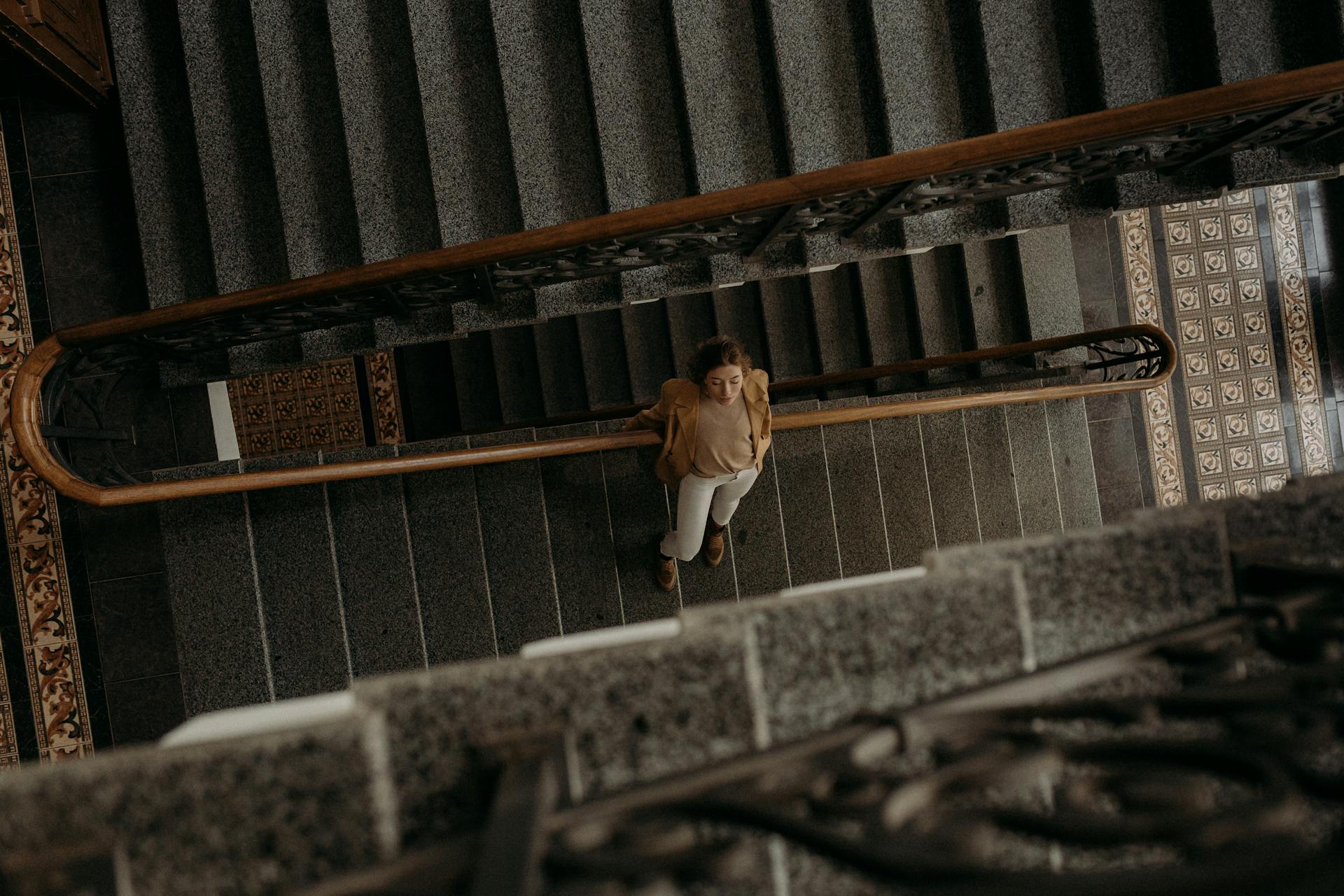 A woman in a blazer descends an elegant staircase, captured from a high angle.