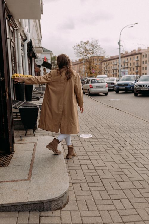 Free Rear view of woman in brown coat walking on city sidewalk in overcast weather. Stock Photo