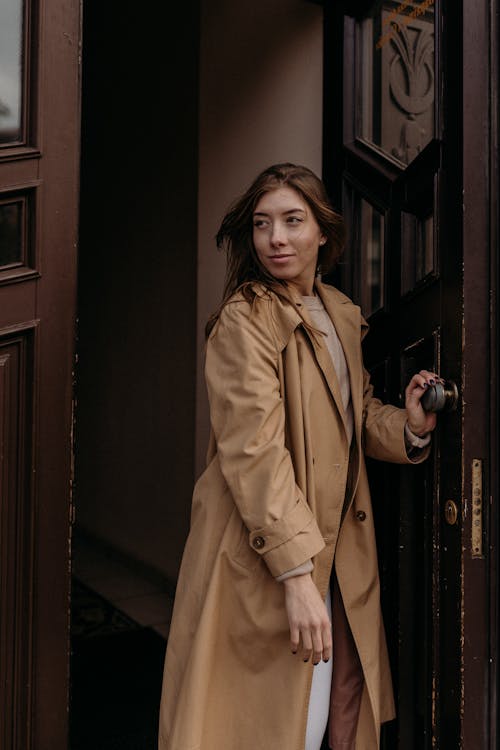 A Woman in Brown Coat is Standing Near Brown Wooden Door