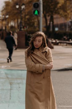 A woman in a trench coat walks in an urban setting on a chilly fall day.