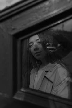 Artistic black and white portrait of a woman reflected in a window, adding urban charm.