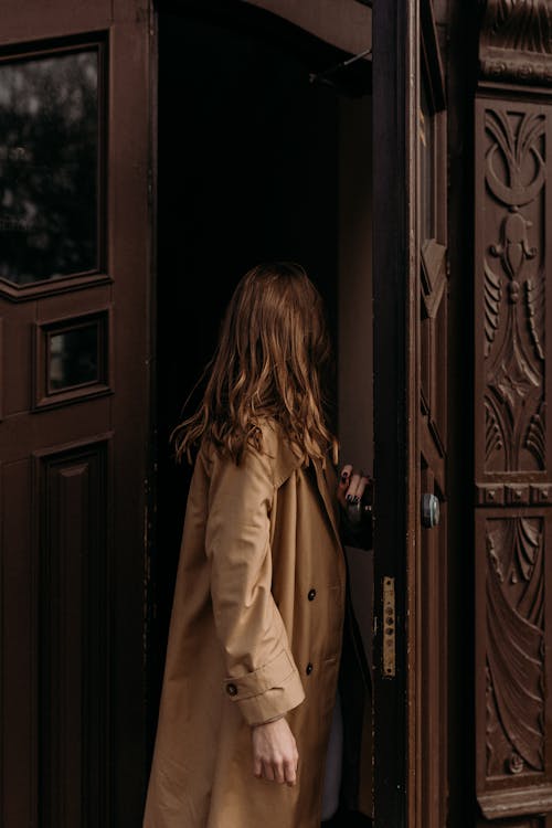 A Woman Wearing Brown Coat Entering a Wooden Door