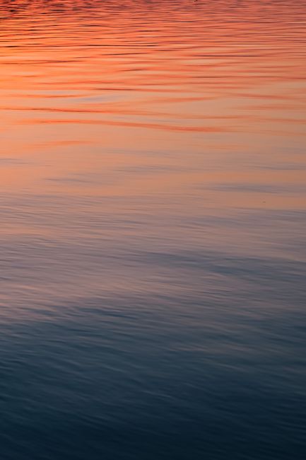 A serene view of sunset reflecting vibrant colors on a calm lake surface.
