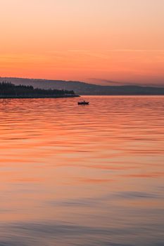 Tranquil sunset with a silhouette of a boat on calm ocean waters, creating a serene seascape.