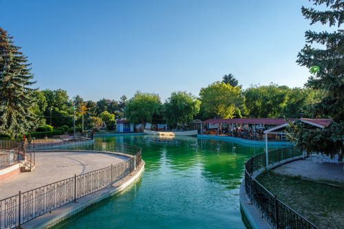 Free Picturesque pond with railings in a summer public park surrounded by trees. Stock Photo