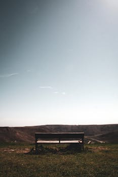 Wooden bench on grassy field with blue sky in Soria, Spain; perfect for serene relaxation.
