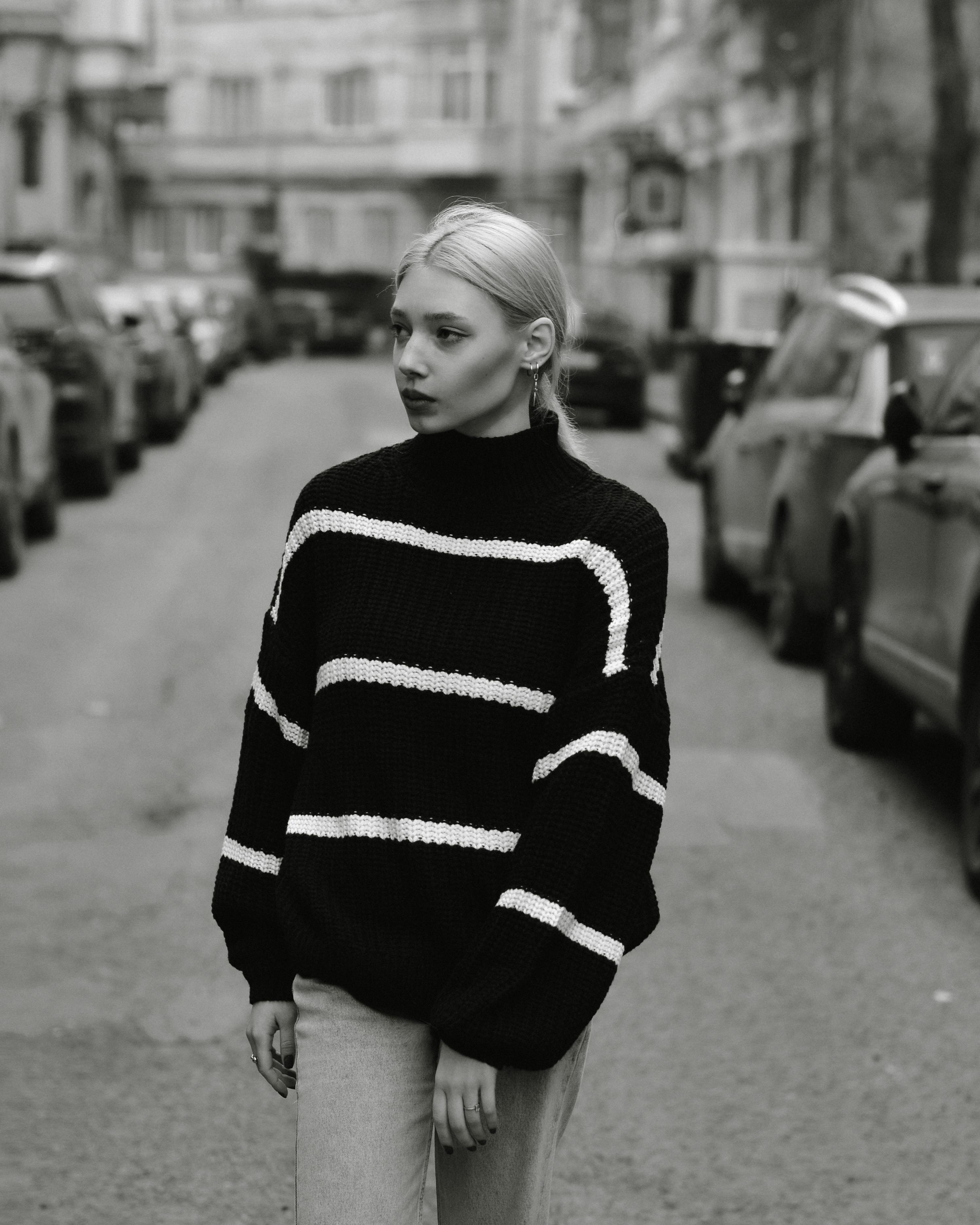 A fashionable woman in a striped sweater walks down a city street in black and white.