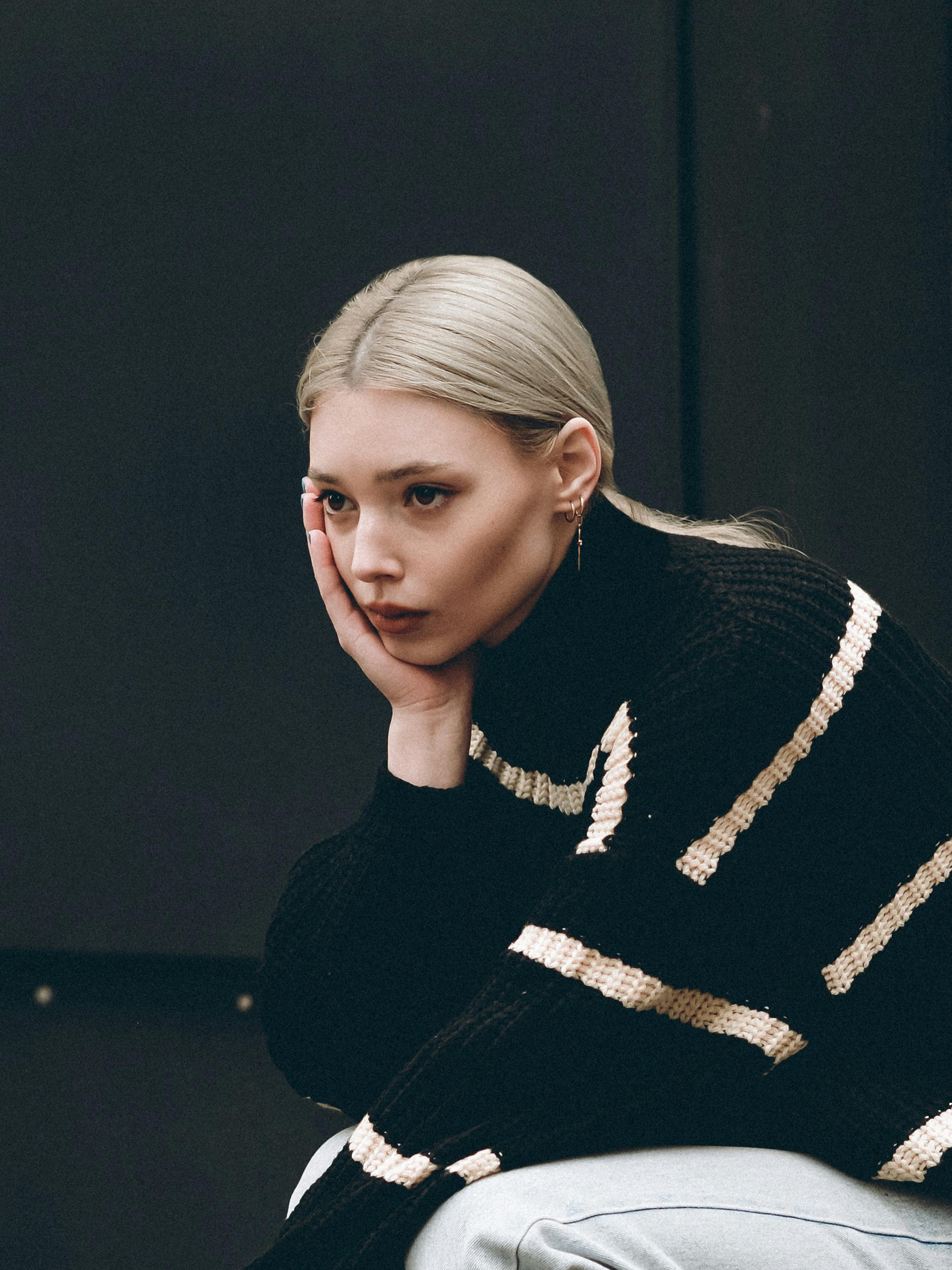 Portrait of a thoughtful woman with blonde hair, in a black striped sweater indoors.