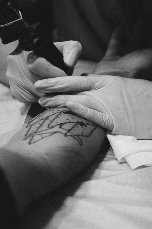 Free Close-up black and white photo of a tattoo artist working on an arm in a studio. Stock Photo