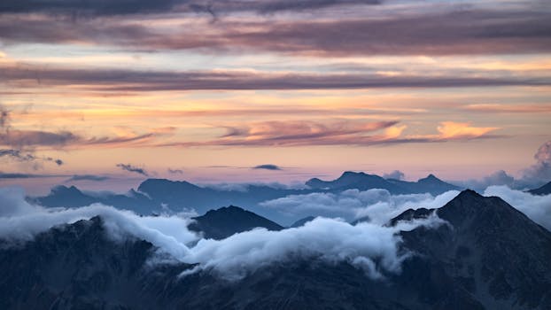 Breathtaking view of mountain peaks shrouded in clouds at sunset. Ideal for landscape and nature enthusiasts.