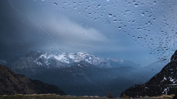 Snow-capped mountains viewed through a windshield with raindrops creating a dramatic scene.