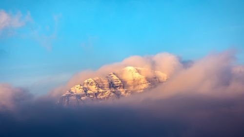 Free Majestic alpine mountain peak bathed in sunrise hues with clouds enveloping the summit, creating a serene landscape. Stock Photo