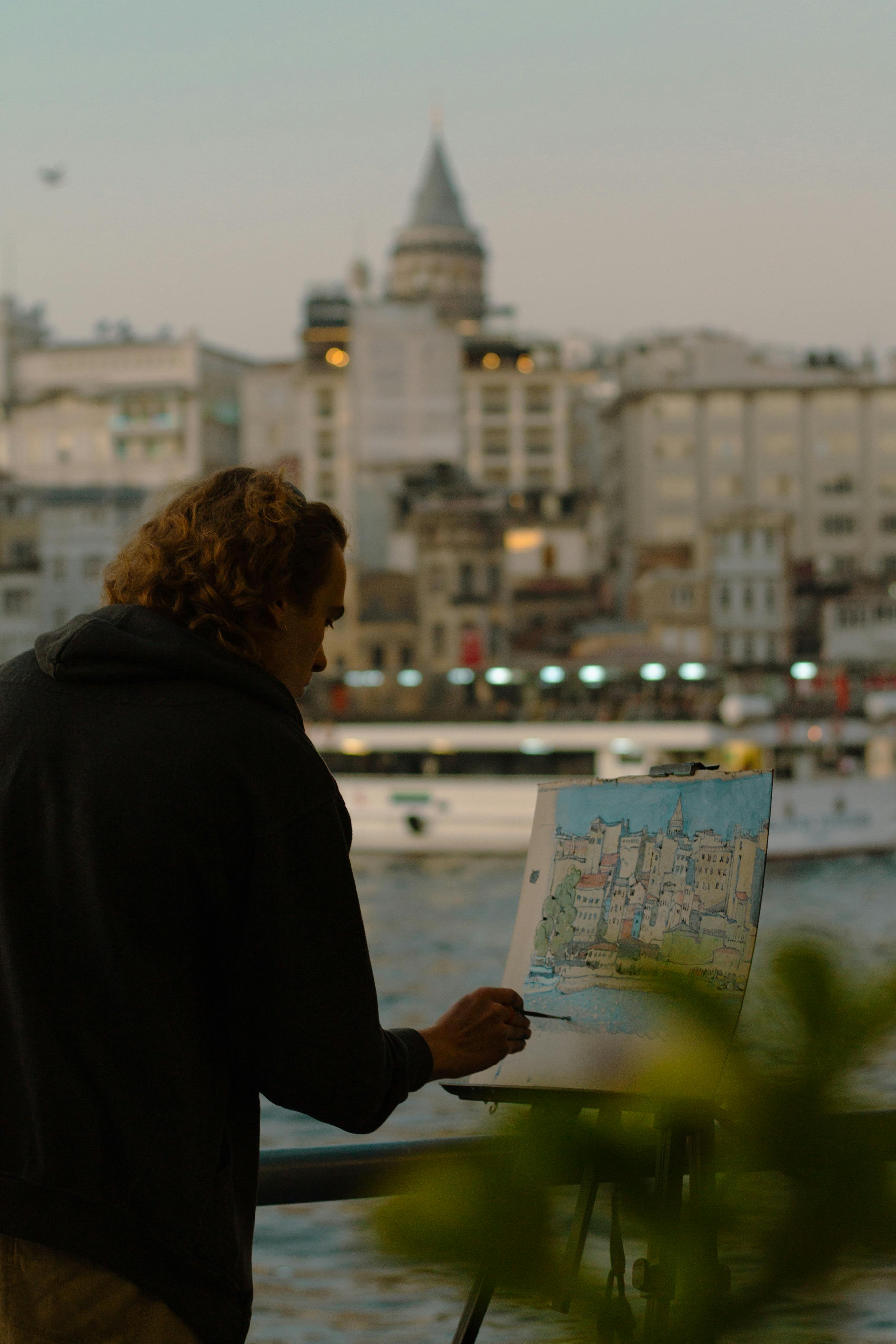 Street artist paints Istanbul cityscape with Galata Tower visible in background.