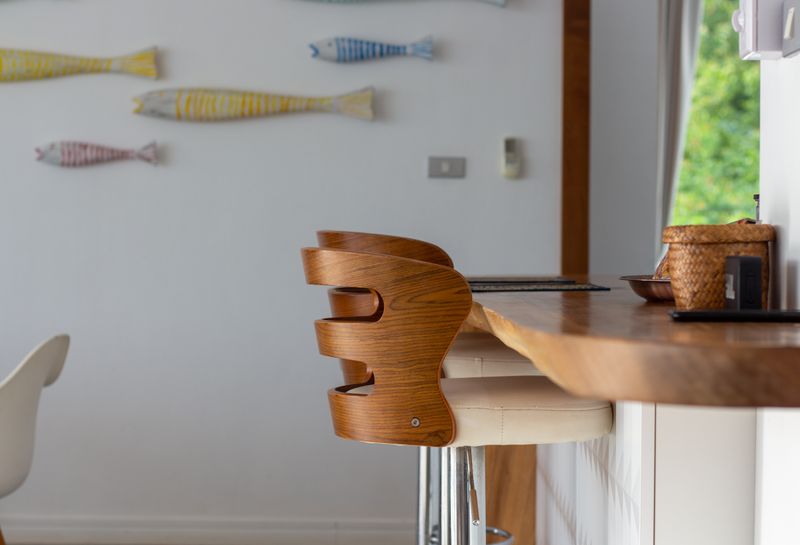 Banqueta alta de madera junto a barra de cocina con decoración de pez en la pared