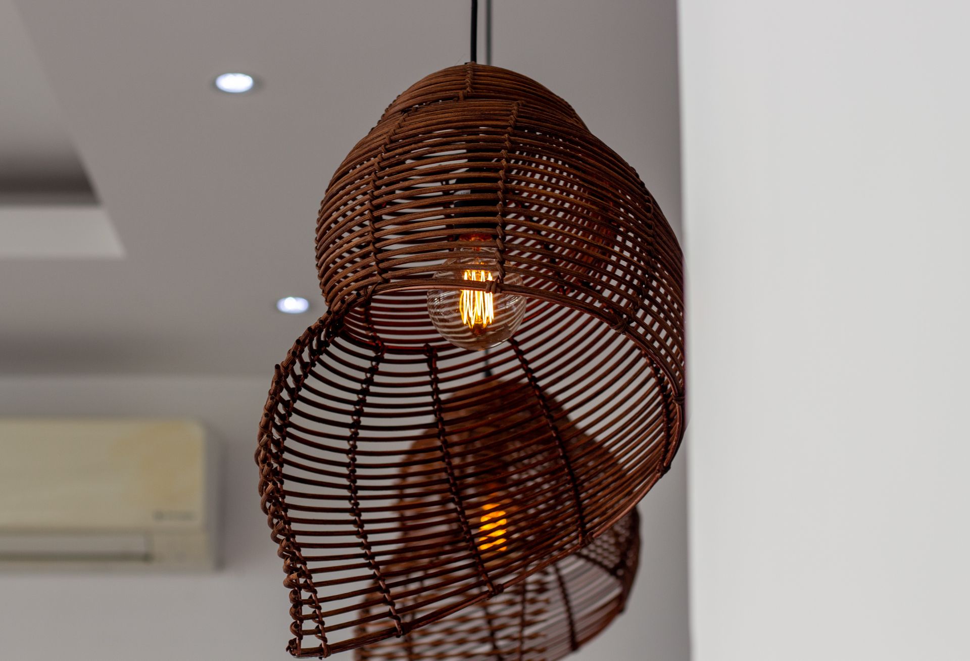 Close-up of a woven rattan pendant light illuminating a modern room interior.