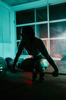A woman preparing to lift weights at a gym under dramatic lighting, showcasing strength and determination.