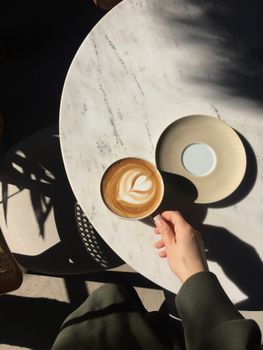 A cozy scene of a latte with art on a marble table, basking in the sunlight.