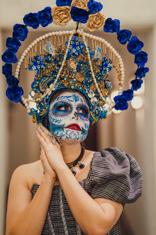 Free A stunning portrait of a woman in traditional Dia de los Muertos makeup and attire, featuring a colorful headdress. Stock Photo
