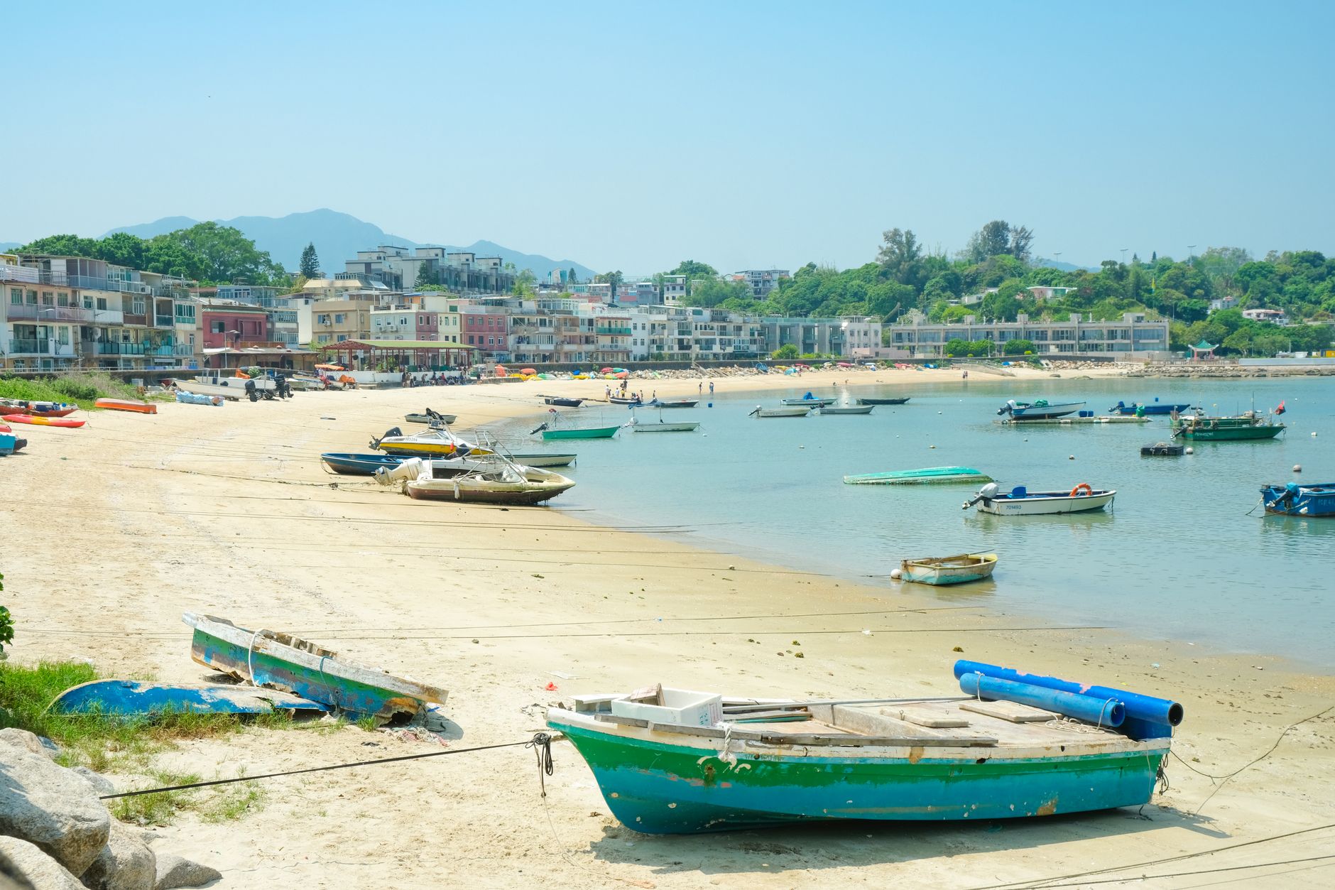 A tranquil seaside scene in Hong Kong, featuring boats on a sandy beach with a coastal village in the background.