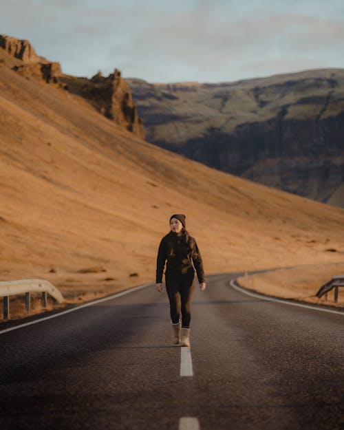 Photo of a Woman in Black Clothes Walking on a Road