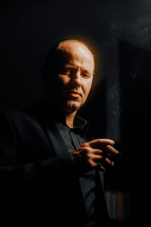 Free A bald man in a suit smokes a cigar against a black background, exuding mystery and elegance. Stock Photo