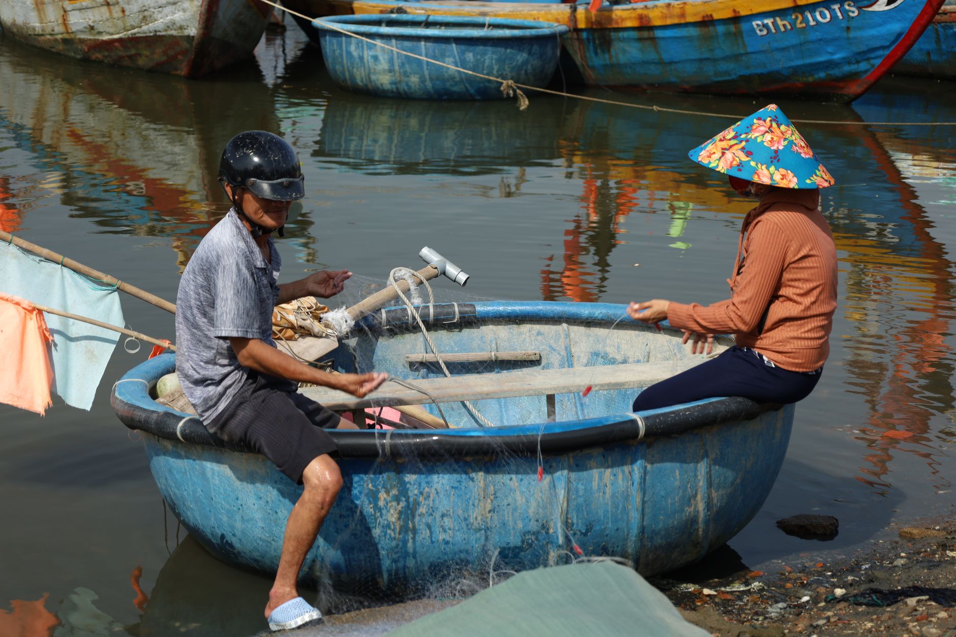 Dos personas pescando en un tradicional bote canasta redondo en un río tranquilo.