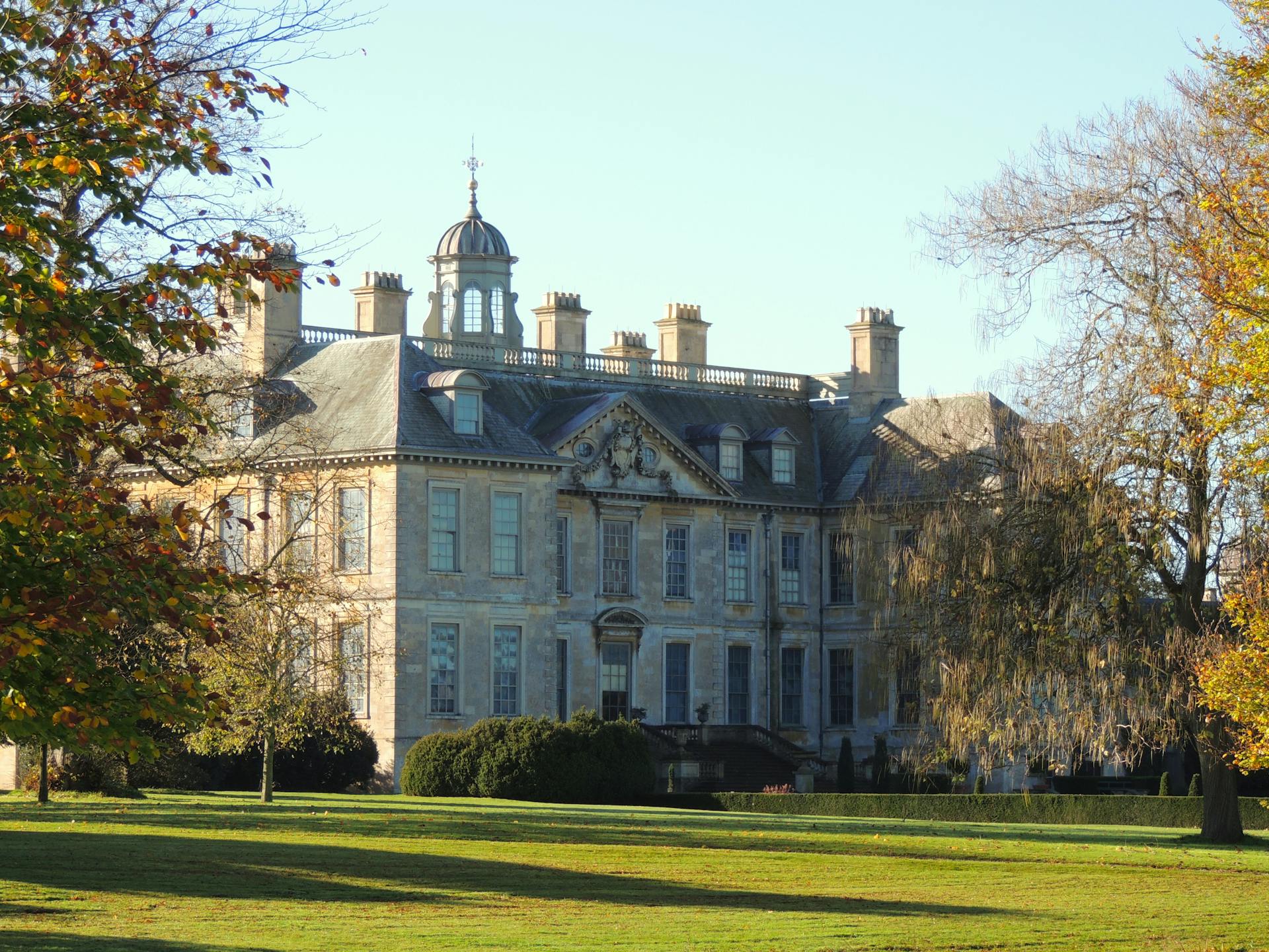 A grand historic manor surrounded by lush gardens and autumn foliage.